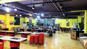 A spacious indoor area with tables and chairs, a kitchen area, and a seating area with red stools. - Sanbangsan Parktel - Hostel (Seogwipo)