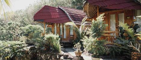 A wooden cabin with a red roof, surrounded by lush greenery and a stone pathway.