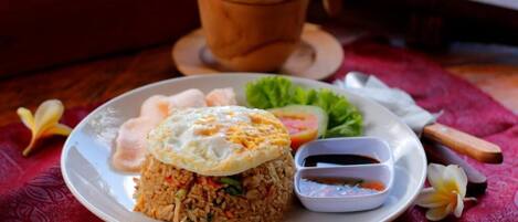 A plate of fried rice with an egg on top, a small bowl of sauce, and a side of fresh vegetables.