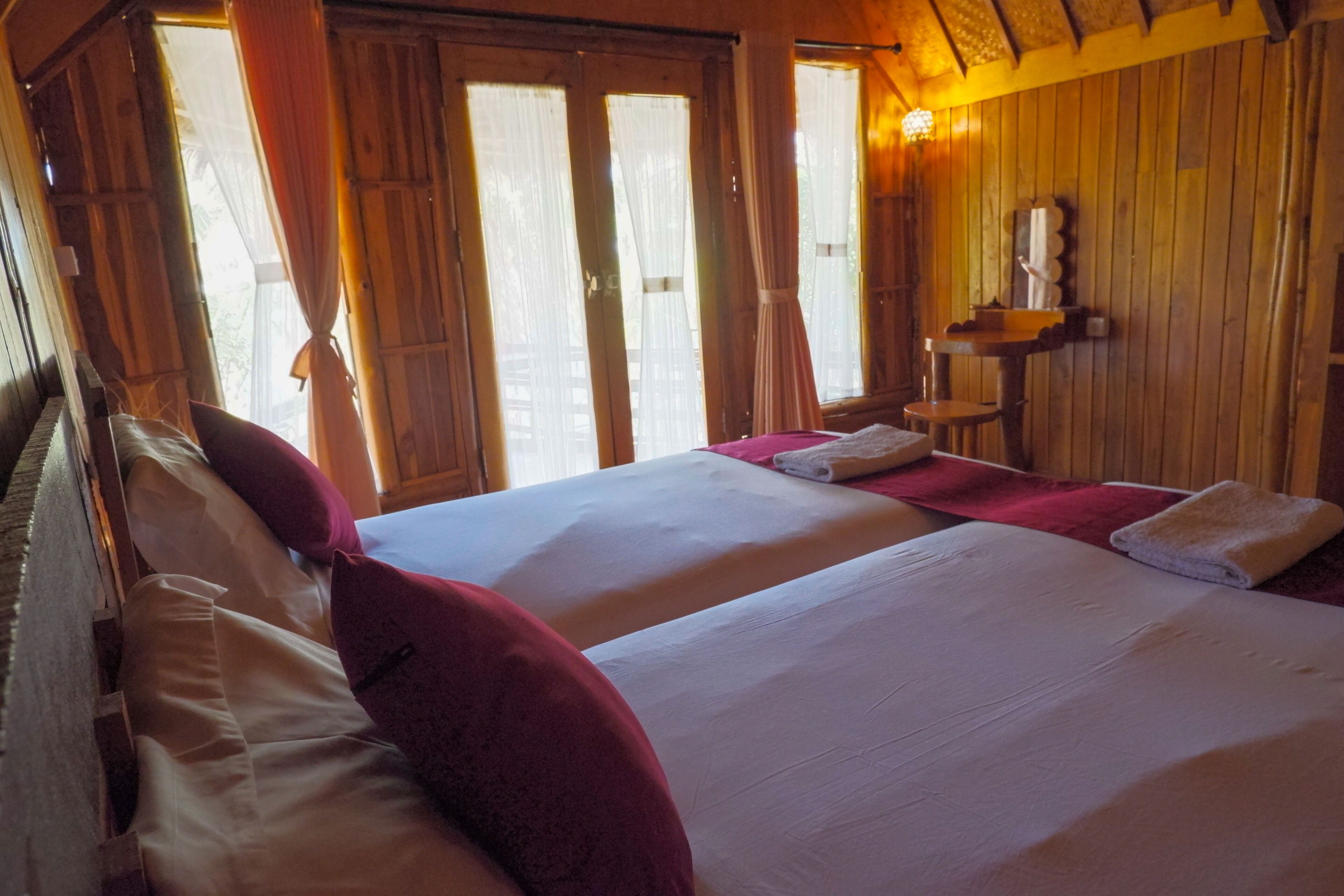 Habitación con dos camas, paredes de madera y una ventana con cortinas.