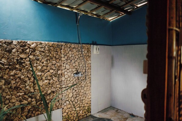 Un área de ducha pequeña y cerrada con pared de piedra y pared de azulejos blancos.
