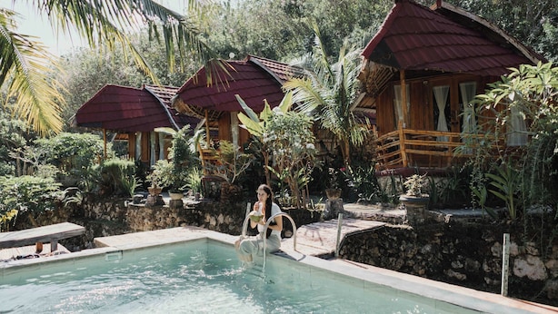 Un área de piscina con cabañas de madera, rodeada de exuberante vegetación.