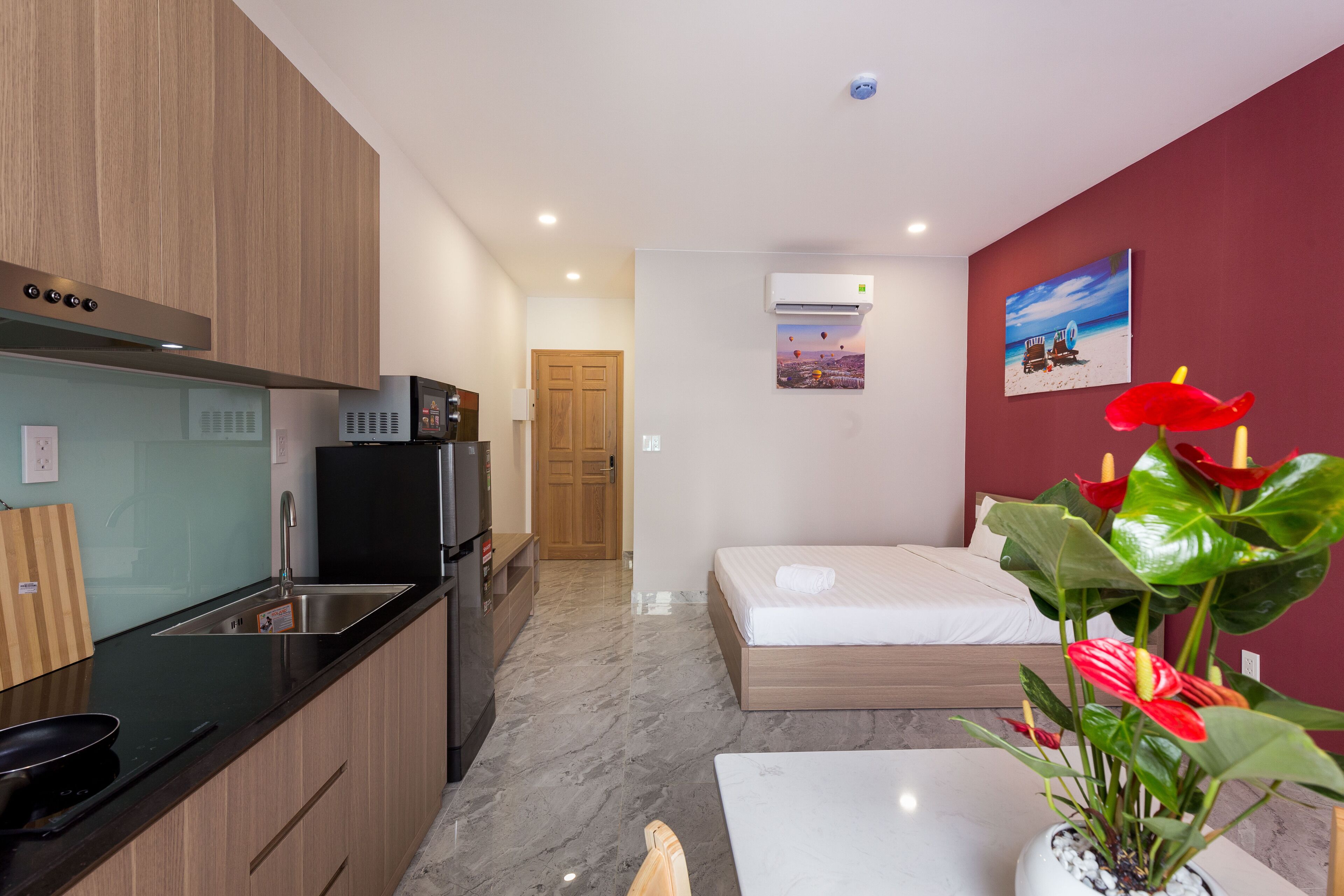 Una habitación de hotel compacta con kitchenette, una cama, una mesita y una planta en maceta.
