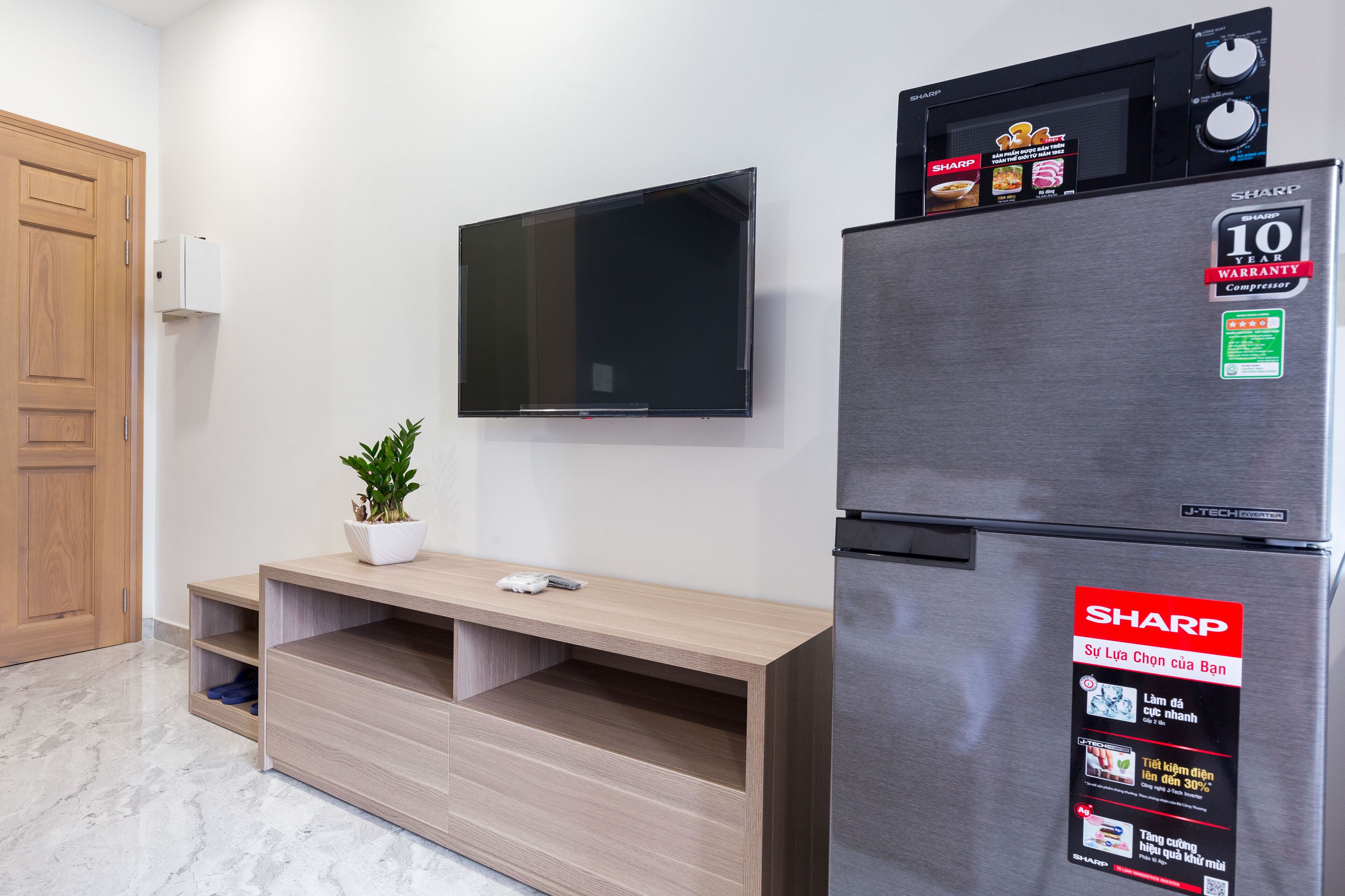 Ett modernt kök med ett kylskåp i rostfritt stål, en platt-TV som är monterad på väggen och ett träskåp med en krukväxt ovanpå.