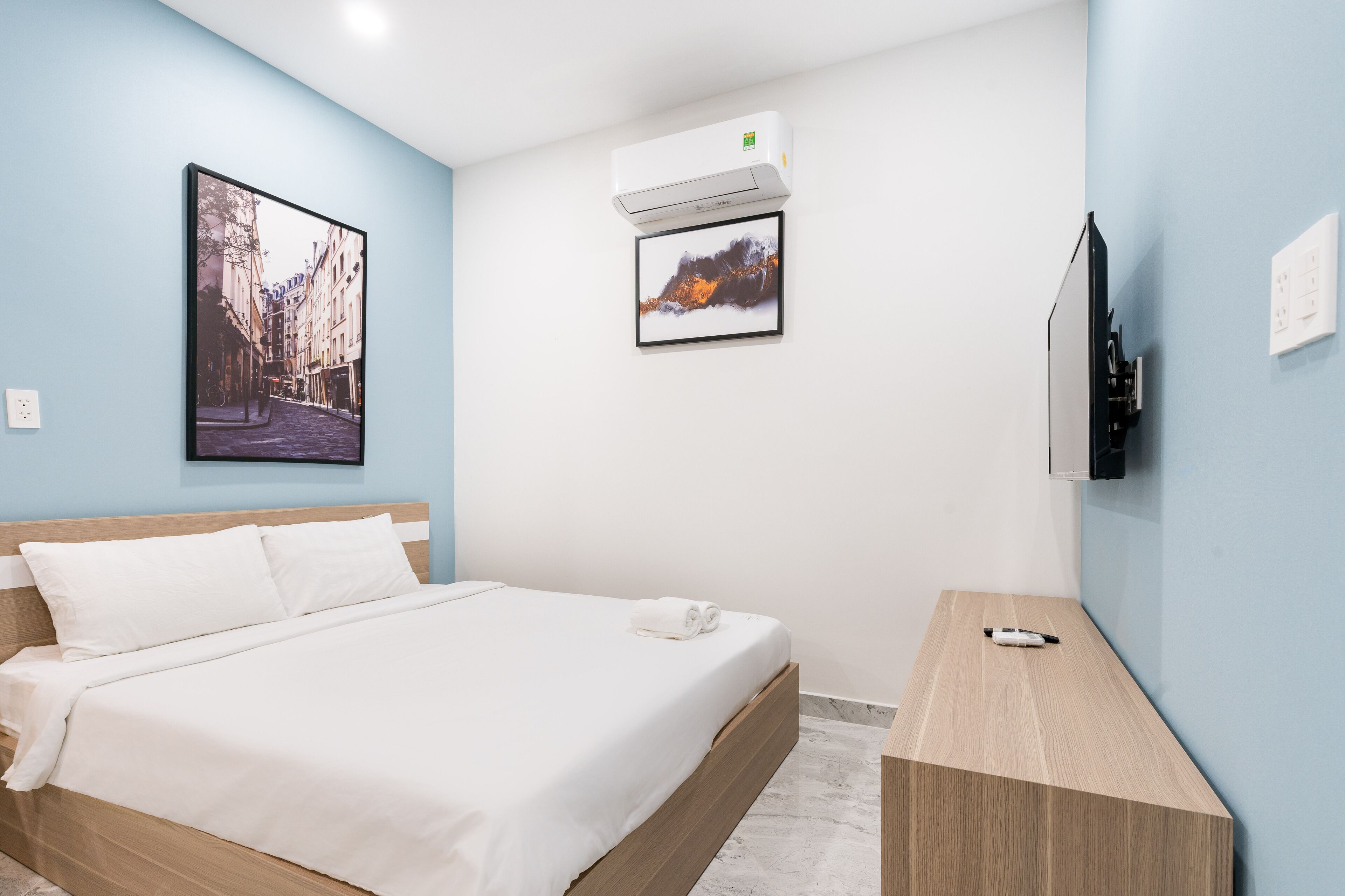 A hotel room with a bed, a wooden nightstand, a TV, and two framed pictures on the wall.
