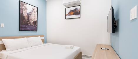 A hotel room with a bed, a wooden nightstand, a TV, and two framed pictures on the wall.