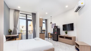 A modern hotel room with a large bed, a TV, a mini-fridge, and a balcony with a view.