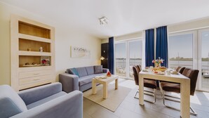 Un salon moderne comprenant un canapé, une table à manger avec des chaises, un meuble en bois et une grande fenêtre avec des rideaux.