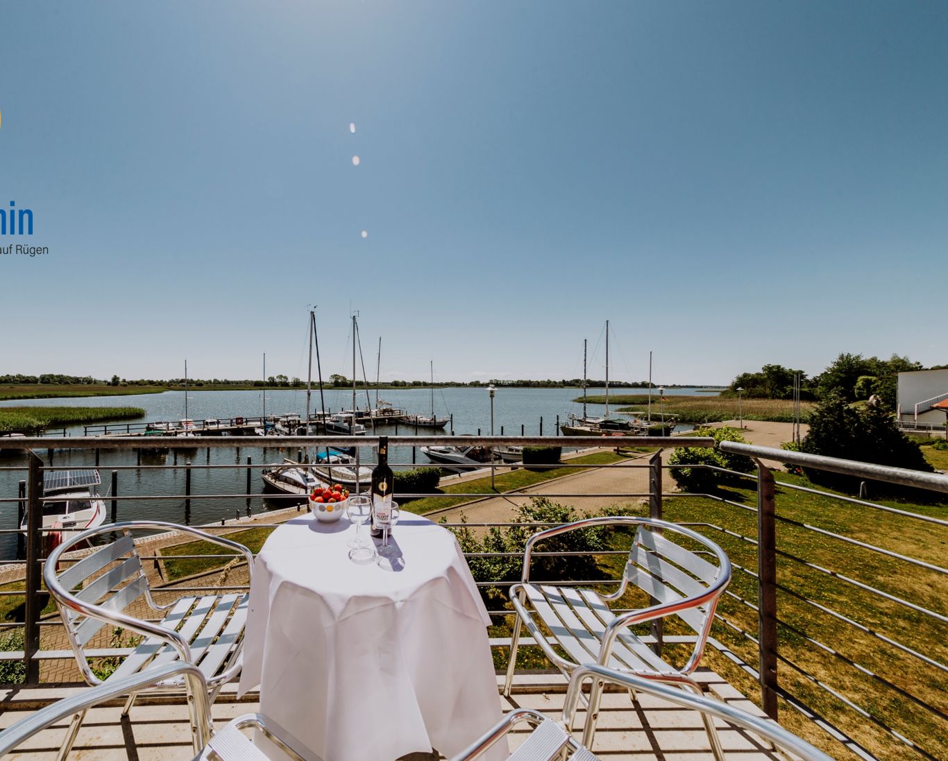 Een eethoek met een tafel gedekt voor twee, met uitzicht op een jachthaven met boten en een rustig wateroppervlak.