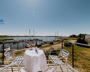 Un comedor con una mesa dispuesta para dos personas, con vistas a un puerto deportivo con barcos y una masa de agua tranquila.
