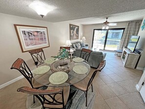 A dining area with a glass table, chairs, and a view of the living room.