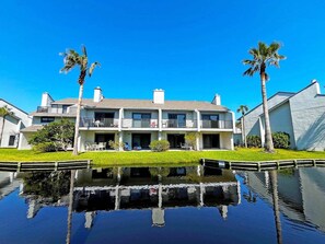 A two-story residential building with a balcony, a swimming pool, and palm trees.
