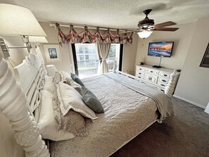 A bedroom with a bed, a dresser, a ceiling fan, a TV, and a window with curtains.
