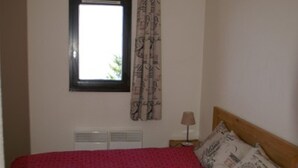 A bedroom with a bed, a window with curtains, a nightstand with a lamp, and a radiator.