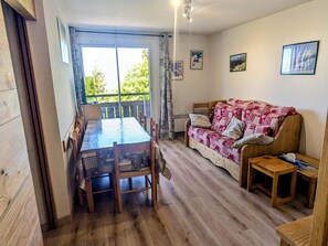 A room with a wooden dining table, chairs, a patterned sofa, and a small wooden side table.
