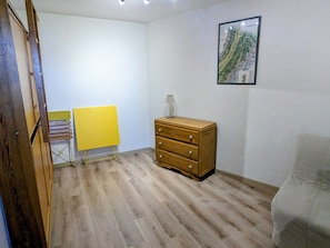 Um quarto com cômoda de madeira, uma cadeira dobrável amarela e um quadro na parede.