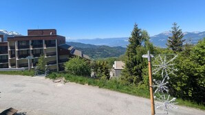 A building with multiple balconies, a clear view of the mountains, and a gravel parking area.