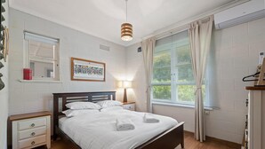 A neatly made bed with white linens, a bedside table with a lamp, and a window with curtains.