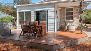 A small house with a deck, a dining table with chairs, and a large barrel.