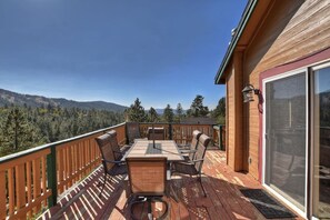 A wooden deck with a table and chairs, overlooking a forested mountain range.