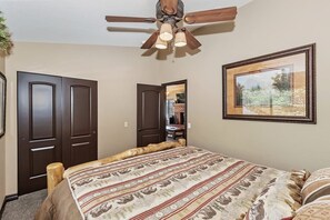 A bedroom with a bed, a ceiling fan, a framed picture on the wall, and a door leading to another room.