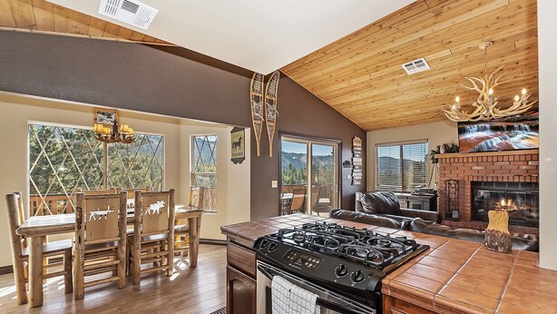 A kitchen with a gas stove, wooden dining table, and chairs. There is a fireplace with a brick surround and a mounted television.