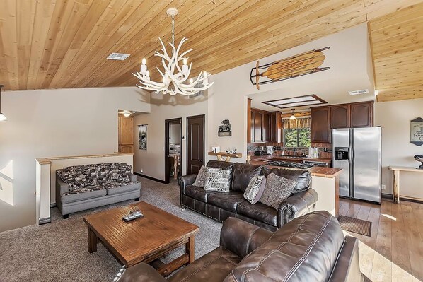 A spacious living room with a fireplace, leather sofas, and a wooden ceiling.