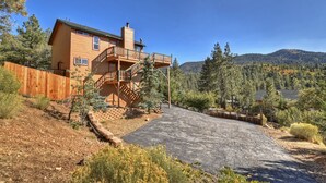 A two-story wooden house with a balcony, surrounded by a wooden fence and a gravel driveway.