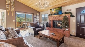 A cozy living room with a fireplace, leather sofa, and a large window overlooking a scenic view.