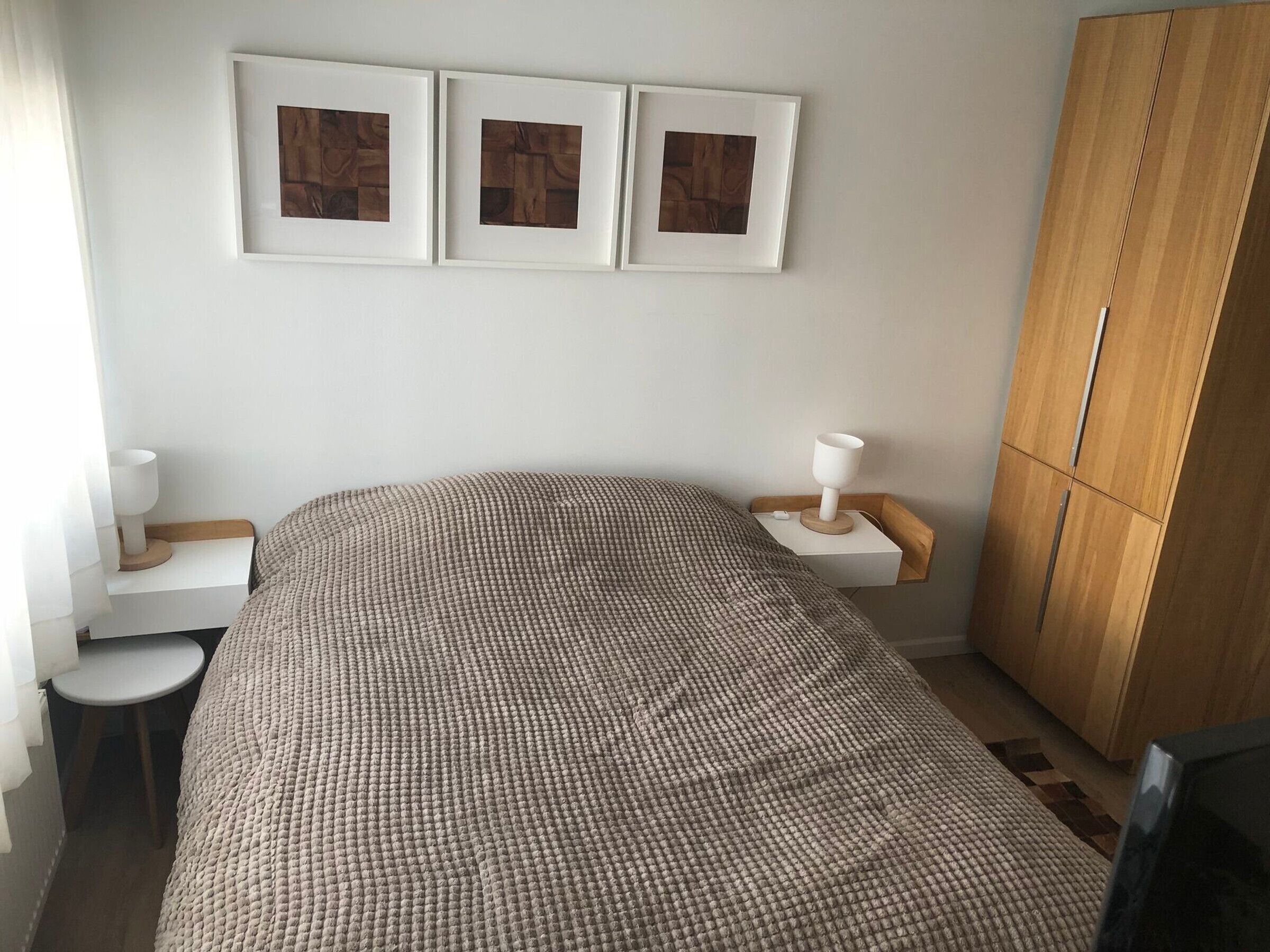 Ein Schlafzimmer mit Bett, Nachttischen, einem Kleiderschrank und gerahmten Bildern an der Wand.