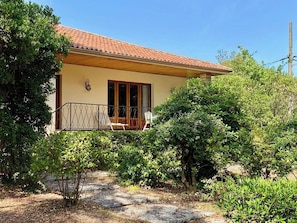 A house with a tiled roof, a balcony with a metal railing, and a garden with various shrubs and a tree.