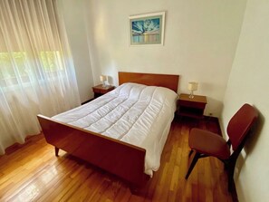 Ein Schlafzimmer mit einem hölzernen Bett, einem Nachttisch, einem Stuhl und einem Bild an der Wand.
