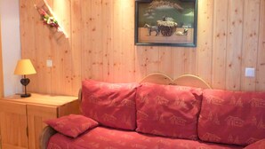 Une pièce aux murs lambrissés, avec un canapé rouge, une petite table de chevet dotée d’une lampe et un tableau encadré accroché au mur.