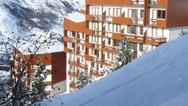 Un bâtiment moderne à plusieurs étages, doté d’une façade en bois, entouré de montagnes enneigées.