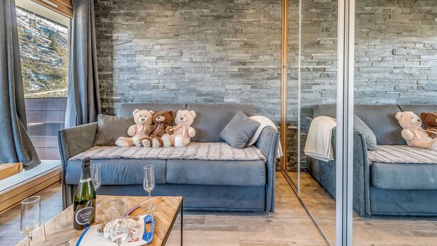 A modern living room with a stone wall, a grey sofa, and two plush teddy bears. - Renovated Studio 4 pax - Ski-in/Ski-out with WiFi (Tignes-Le Lavachet)