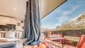 A modern kitchen with white cabinets, a dining area with a table and chairs, and a large window with a view of a snowy mountain. - Renovated Studio 4 pax - Ski-in/Ski-out with WiFi (Tignes-Le Lavachet)