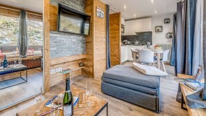 A modern interior with a stone fireplace, wooden walls, a dining area, and a kitchen. - Renovated Studio 4 pax - Ski-in/Ski-out with WiFi (Tignes-Le Lavachet)