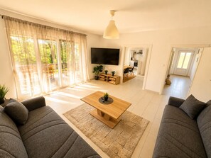 A modern living room with a sofa set, a coffee table, a TV, and a dining area with chairs and a table.