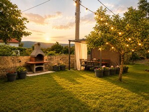 A backyard with a stone oven, outdoor seating, string lights, and potted plants.