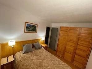 A bedroom with a bed, two bedside lamps, a wooden wardrobe, and a framed picture on the wall.