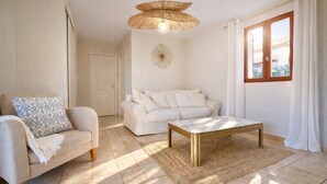 A living room with a sofa, a coffee table, a patterned throw pillow, a woven rug, a decorative wall piece, and a window with curtains. - Charming villa for 4 people, private pool between sea and mountains  (Aléria)