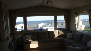 A living room with a sofa, a radiator, and a view of the sea and buildings. - Immaculate 3-bed Caravan in Hartlepool (Hartlepool)