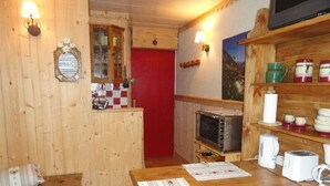 Une cuisine chaleureuse avec des murs en bois, une porte rouge, un four à micro-ondes, une machine à café et une étagère remplie de bocaux.