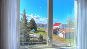 A window with a view of a rural landscape, including a lake, trees, and buildings with red roofs. - 🐾Lakeview on Main - Located in the village of Rangeley with water views! Dog Friendly (Rangeley)