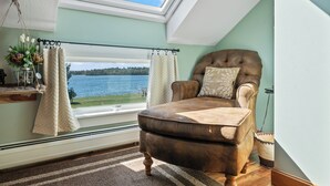A cozy room with a view of a lake, a brown leather armchair, and a window with curtains. - Town Park Condo D - Great central location in the center of downtown Rangeley (Rangeley)