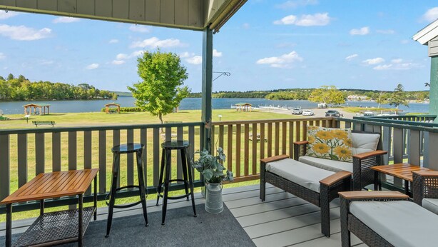 A covered outdoor deck with seating, a view of a lake, and a gazebo in the background. - Town Park Condo D - Great central location in the center of downtown Rangeley (Rangeley)