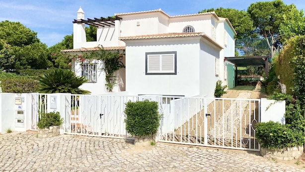 Une villa blanche avec un toit en tuiles, une petite tour et une entrée fermée par un portail.