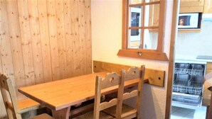 Een houten eettafel met vier stoelen, een raam met uitzicht op een keuken, en een inbouw vaatwasser.