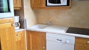 Een kleine keuken met houten kastjes, een magnetron, een spoelbak en een vaatwasser.