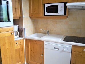 Una cucina compatta con mobili in legno, un forno a microonde, un lavello e una lavastoviglie.